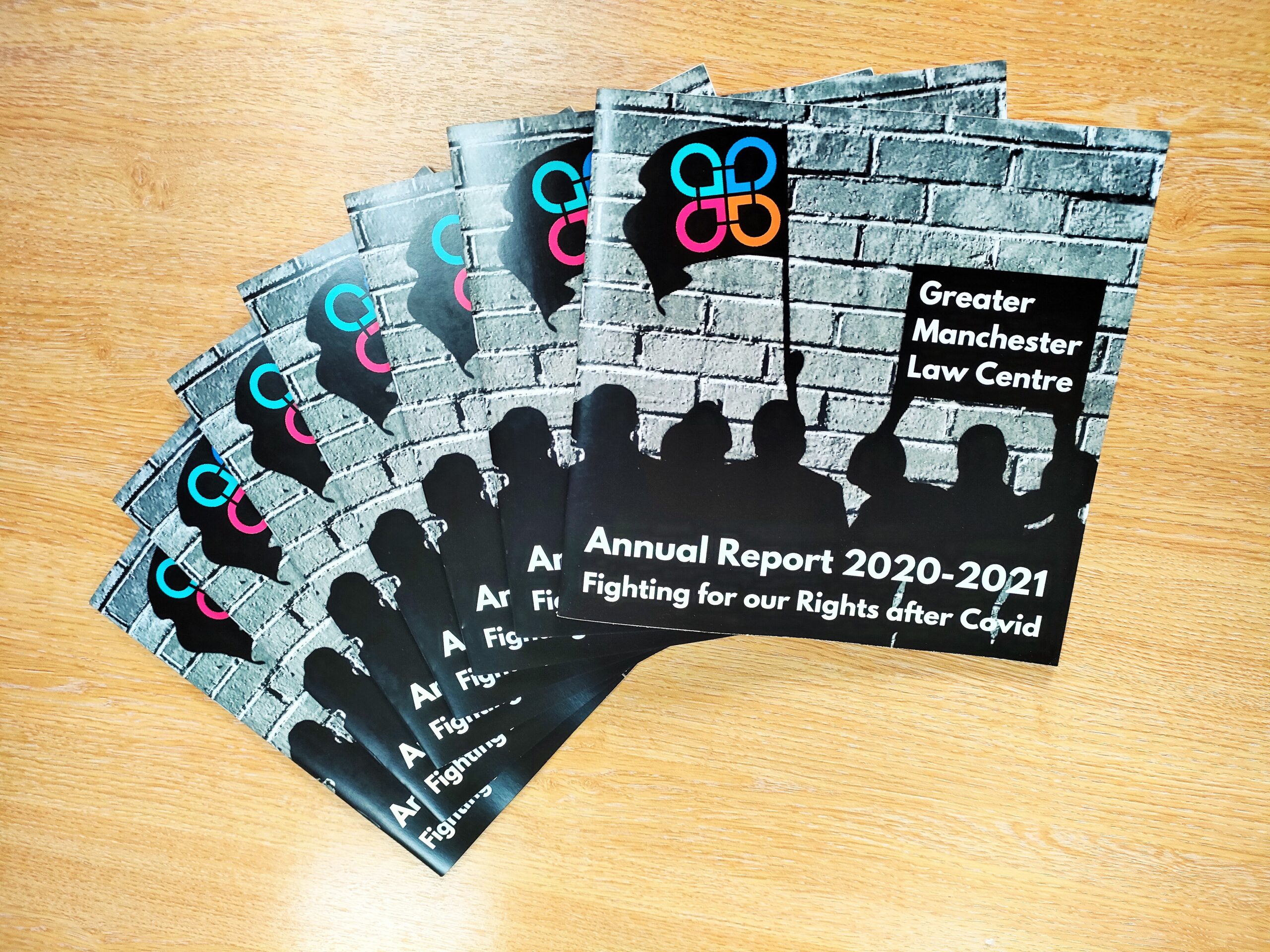 Image shows several copies of GMLC's new Annual Report laid out on a table. Report reads: Fighting for our Rights after Covid, Annual Report 2020-2021.